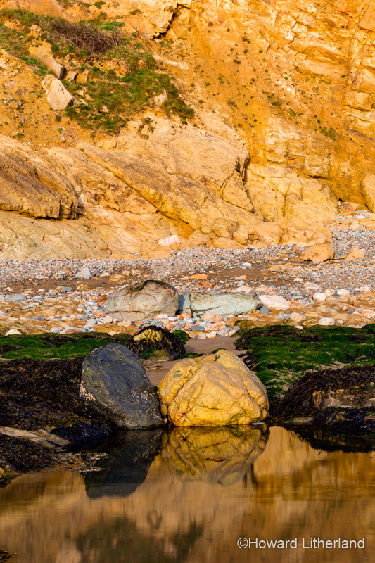 Rocks and cliffs reflecting in a tidal pool on the beach at Church Bay, Anglesey, North Wales
