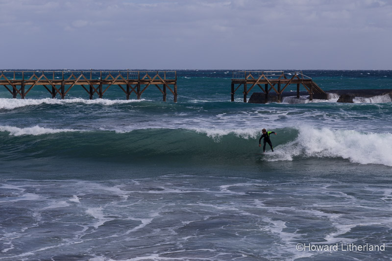 Surfer and broken jetty at Arrieta on the Atlantic coast of Lanzarote in the Canary Islands