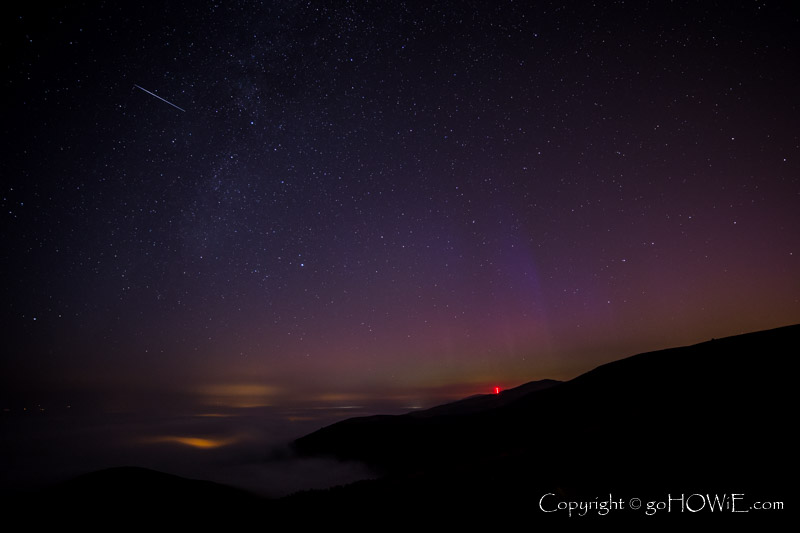 Night time image overlooking the Vale of Clwyd, North Wales showing a blanket of fog over Denbigh, stars, a faint milky way, and a colourful aurora over the Moel Y Parc television transmitter to the north